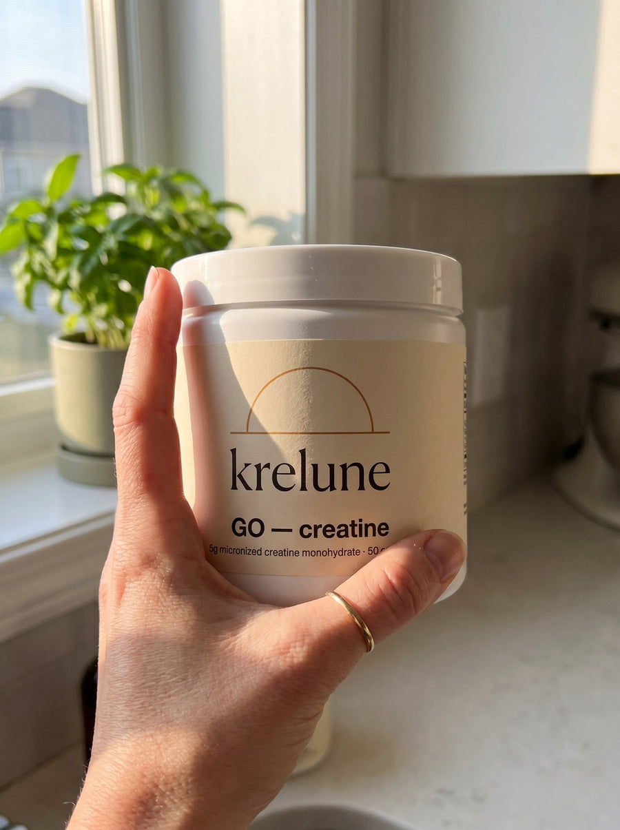 A hand holding the Krelune GO Creatine tub in warm morning window light