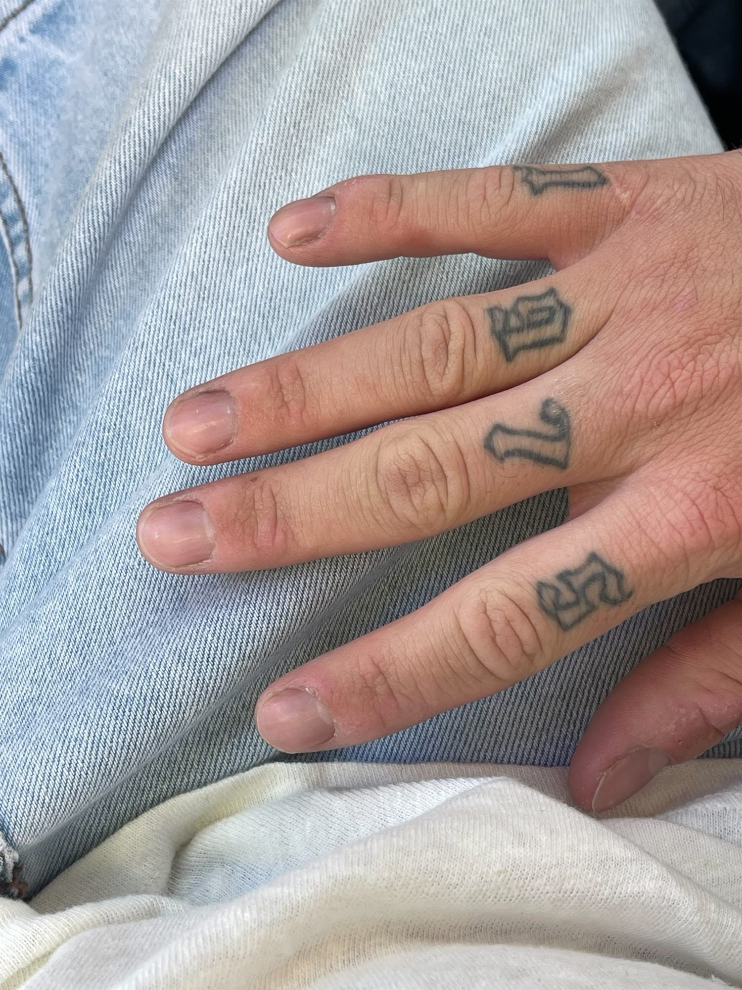 A hand laid flat on denim, all five nails visible, short and bitten with worn cuticles